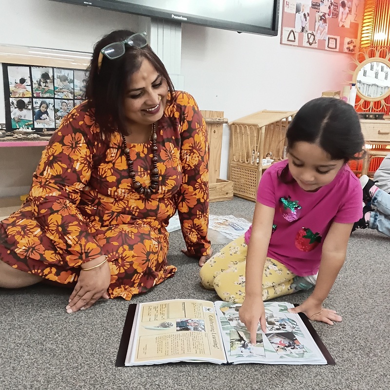 Sudha sits with a young child at our Mount Roskill centre, reading a book together to support early childhood education and literacy